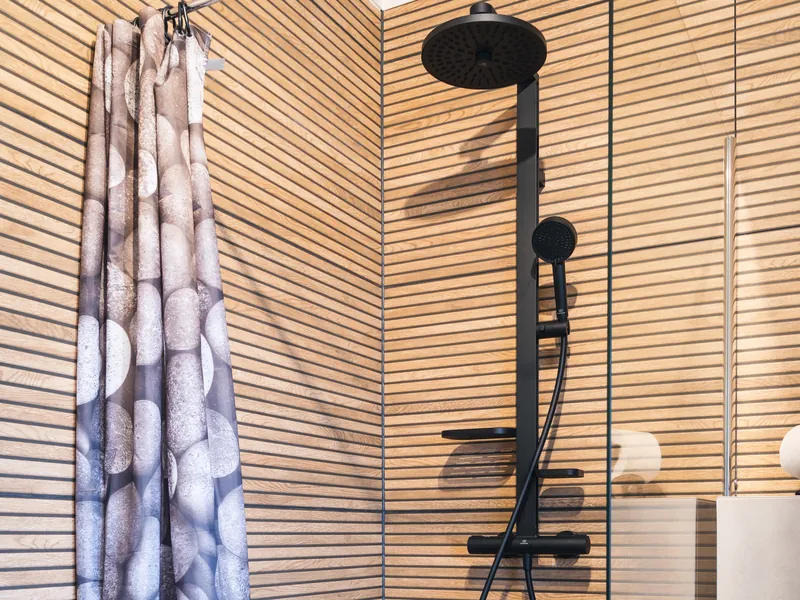 Ebenerdige Dusche mit schwarzer Regendusche und Handbrause vor Wandfliesen in Holzoptik