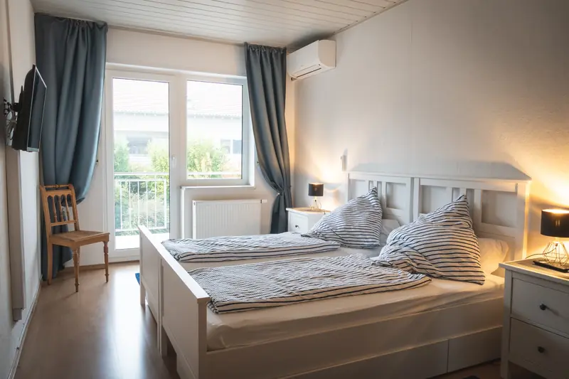 Schlafzimmer mit zwei zusammengestellten Einzelbetten, Nachttischlampen und Balkontür