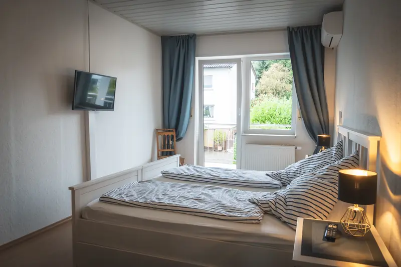 Schlafzimmer mit zwei zusammengestellten Einzelbetten, Klimagerät, Flachbild-TV und Zugang zum Balkon